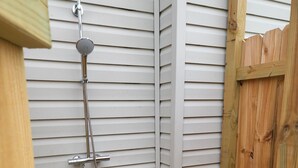 A small, enclosed shower area with a showerhead and hose, wooden steps, and a wooden door.