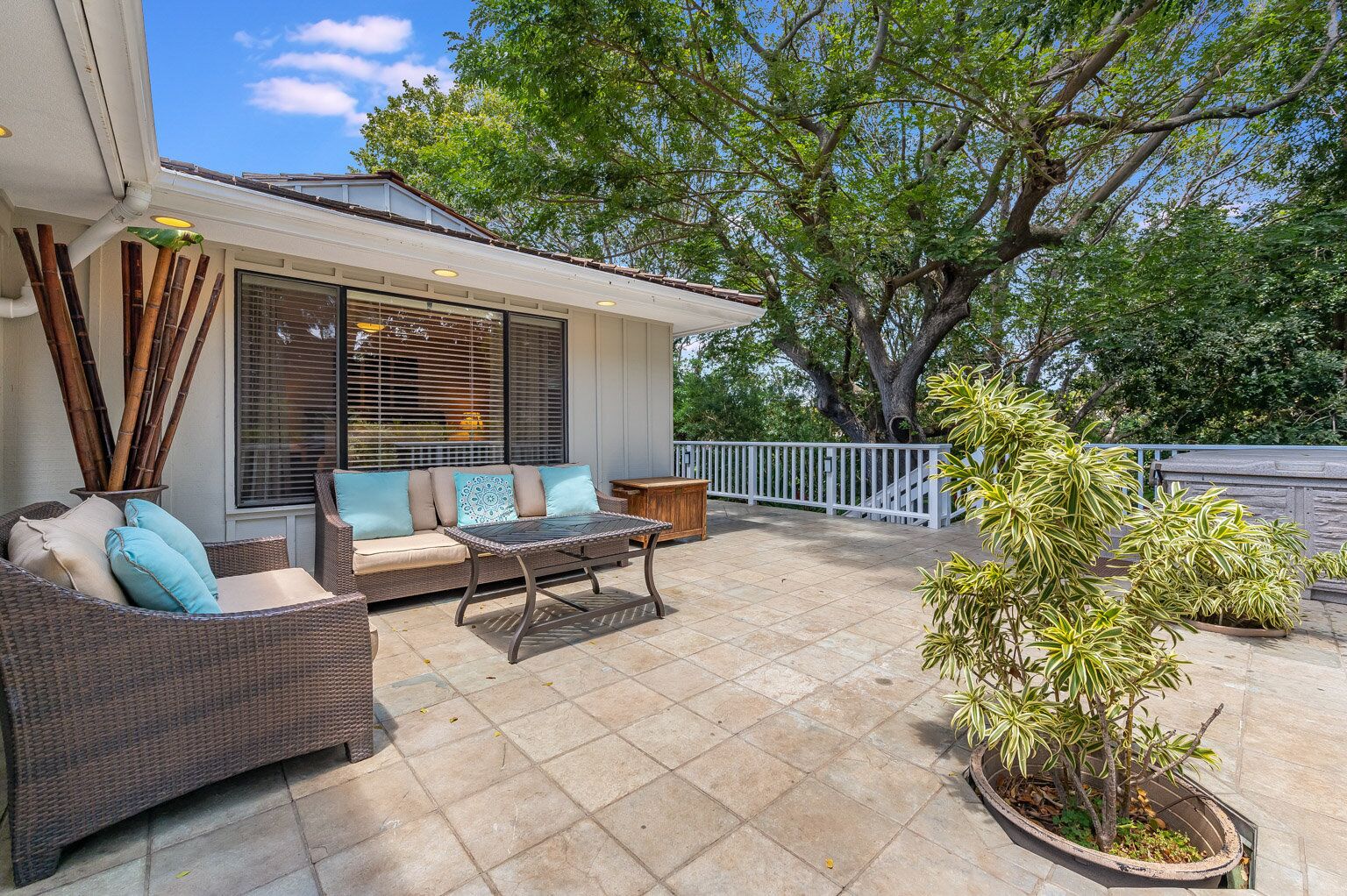 A covered patio with wicker furniture, a potted plant, and a view of a tree.
