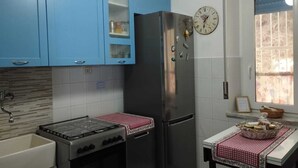 Een keuken met blauwe kastjes, een roestvrijstalen koelkast, een gasfornuis en een raam met uitzicht.