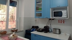 Een keuken met blauwe kastjes, een magnetron en een raam met bloemen gordijnen.