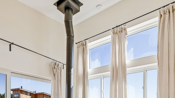 Een moderne woonkamer met een houtkachel, grote ramen en uitzicht op een huis en landschap.