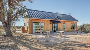 Een moderne houten cabin met een metalen dak, grote schuifdeuren van glas en een terras met zitplaatsen.