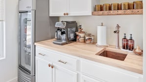 Een moderne keuken met witte kastjes, een roestvrijstalen koelkast, een koffiezetapparaat en houten planken met potten.