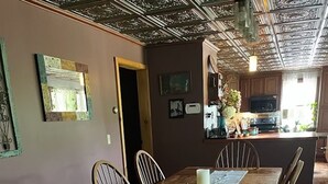 A dining area with a wooden table and chairs, a chandelier, and a kitchen in the background. - Private Adirondack Getaway. Close to hiking trails, fishing, public beach. (Clemons)