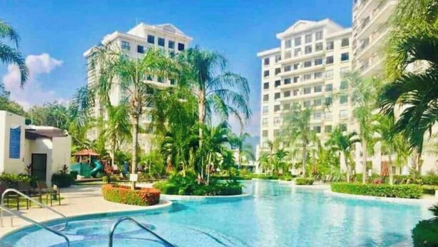 Una piscina con hidromasaje, rodeada de palmeras y edificios modernos.
