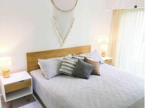 A neatly made bed with a white quilt, several pillows, and a wooden headboard. There are two bedside tables with lamps and a wall-mounted light fixture.