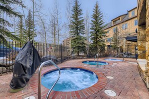 Un espace piscine doté de deux bains à remous, entouré d’une terrasse en briques et d’un mur en pierre.