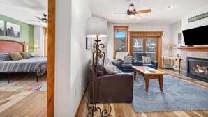 Un salon chaleureux avec une cheminée, un ventilateur de plafond et une grande fenêtre donnant sur des montagnes enneigées.