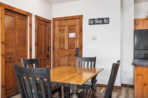 Un coin repas avec une table et des chaises en bois, une enseigne sur laquelle on peut lire « Manger, dormir, skier », et des portes en bois.