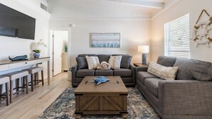 A modern living room with a gray sofa, a wooden coffee table, and a TV on a white wall. - Cute Home with pool, spa, mini golf walk to beach! (Holmes Beach)