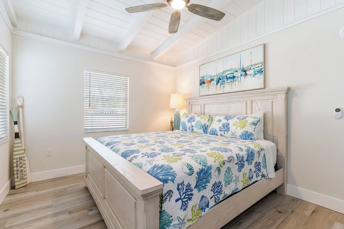 A bedroom with a bed, a ceiling fan, a painting, and a window with blinds.