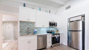 A modern kitchen with white cabinets, a stainless steel refrigerator, a microwave, and a tiled backsplash. - Cute Home with pool, spa, mini golf walk to beach! (Holmes Beach)