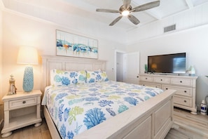 A bedroom with a bed, nightstands, a TV, and a ceiling fan.
