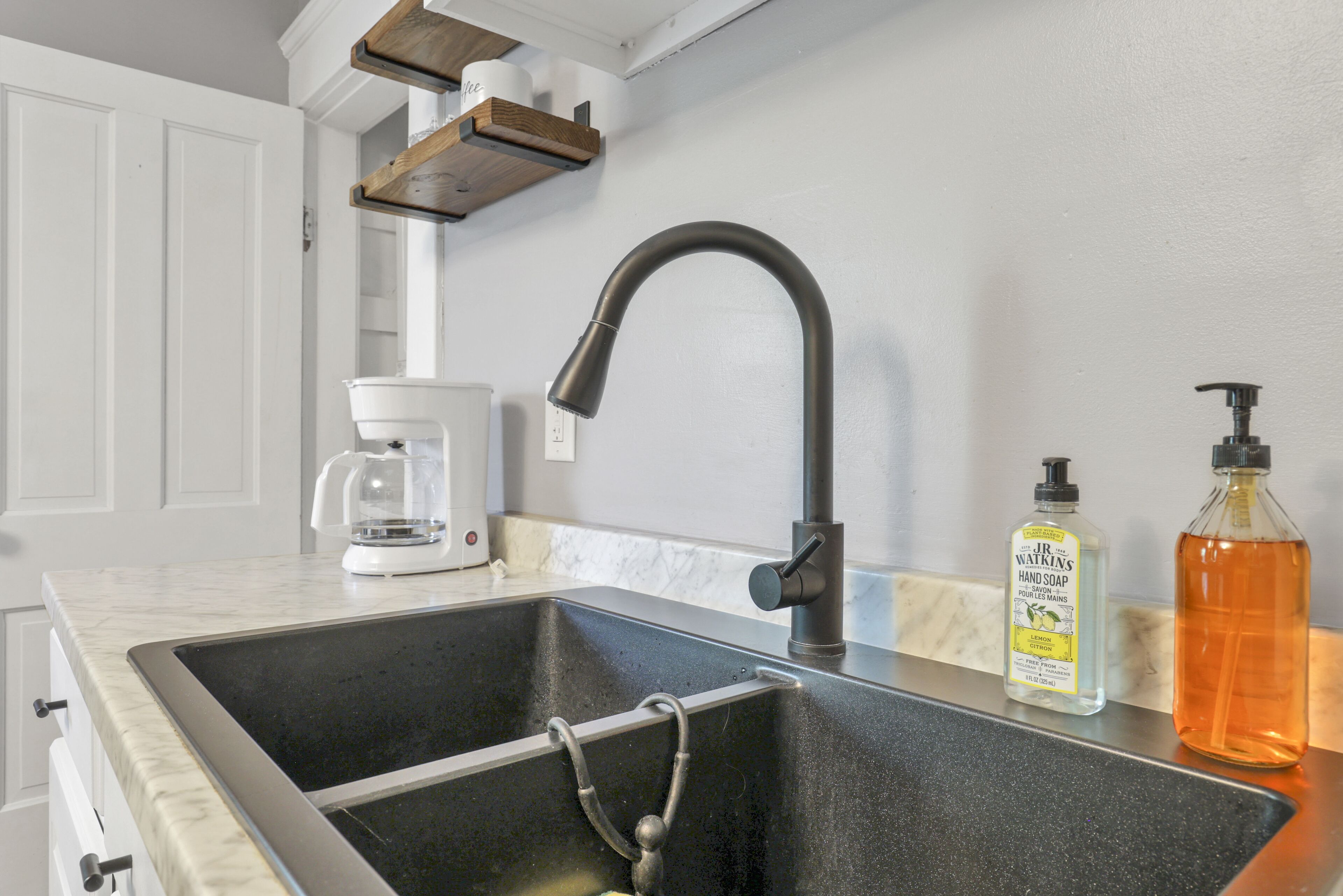 A kitchen with a black sink, a coffee maker, and a bottle of hand soap.