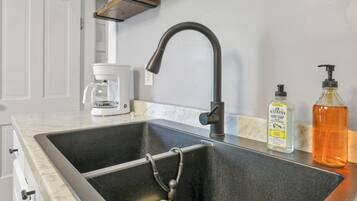 A kitchen with a black sink, a coffee maker, and a bottle of hand soap.