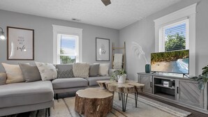 Una sala de estar moderna con un sofá gris, una mesa de centro y un televisor sobre un mueble de madera.