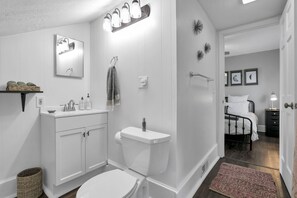 A modern bathroom with a toilet, sink, and mirror. There is a small shelf with decorative items and a basket. - Stylish Small-Town Retreat - Near Lancaster (Baltimore)
