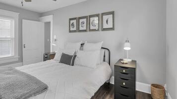 Un dormitorio con cama, mesita de noche, lámpara, ventilador de techo y cuadros en la pared.