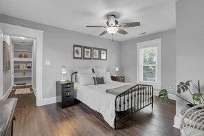 A bedroom with a bed, bedside tables, a ceiling fan, a window with blinds, and a plant. - Stylish Small-Town Retreat - Near Lancaster (Baltimore)