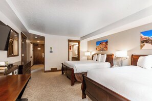A hotel room with two beds, a desk, a mirror, and a door leading to another room.
