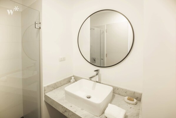 A modern bathroom with a white sink, a round mirror, and a glass shower enclosure. - Modern Lofts in Grau Building by Wynwood-House (Lima)