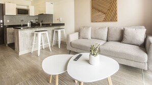 Ein modernes Wohnzimmer mit einem grauen Sofa, zwei weißen runden Tischen und einer Küchenzeile mit Mikrowelle und Barhocker.