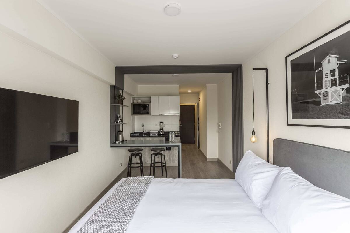 A modern hotel room with a large bed, a small kitchenette, and a dining area.