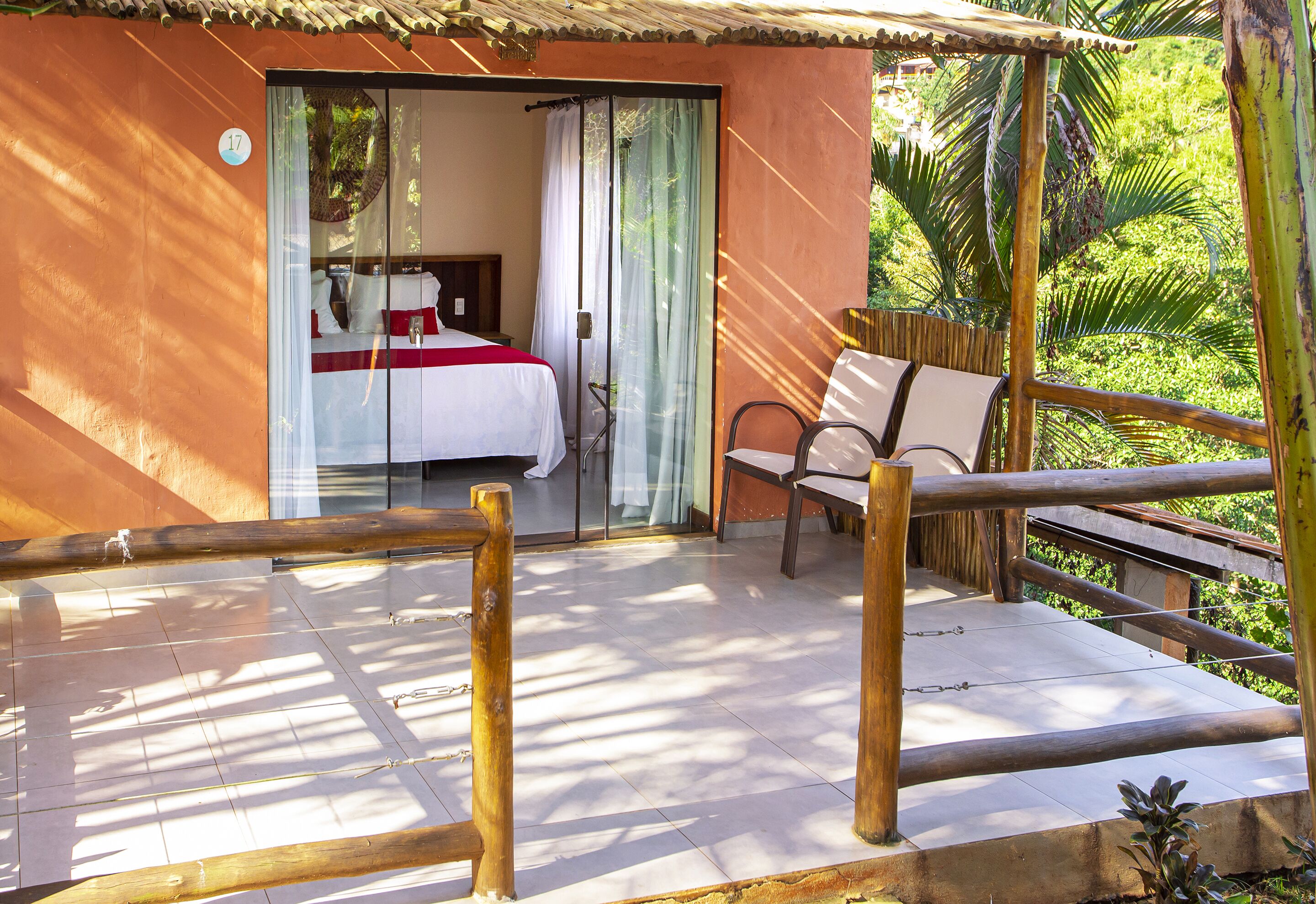 Quarto com cama, cadeira e vista para vegetação.