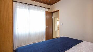 A bedroom with a bed, a wooden door, and a window with sheer curtains.