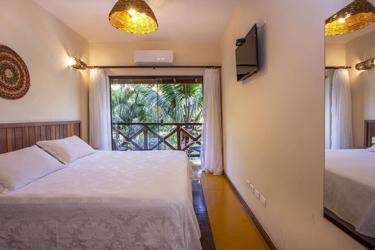 A hotel room with a bed, a television, and a balcony with a view of palm trees.