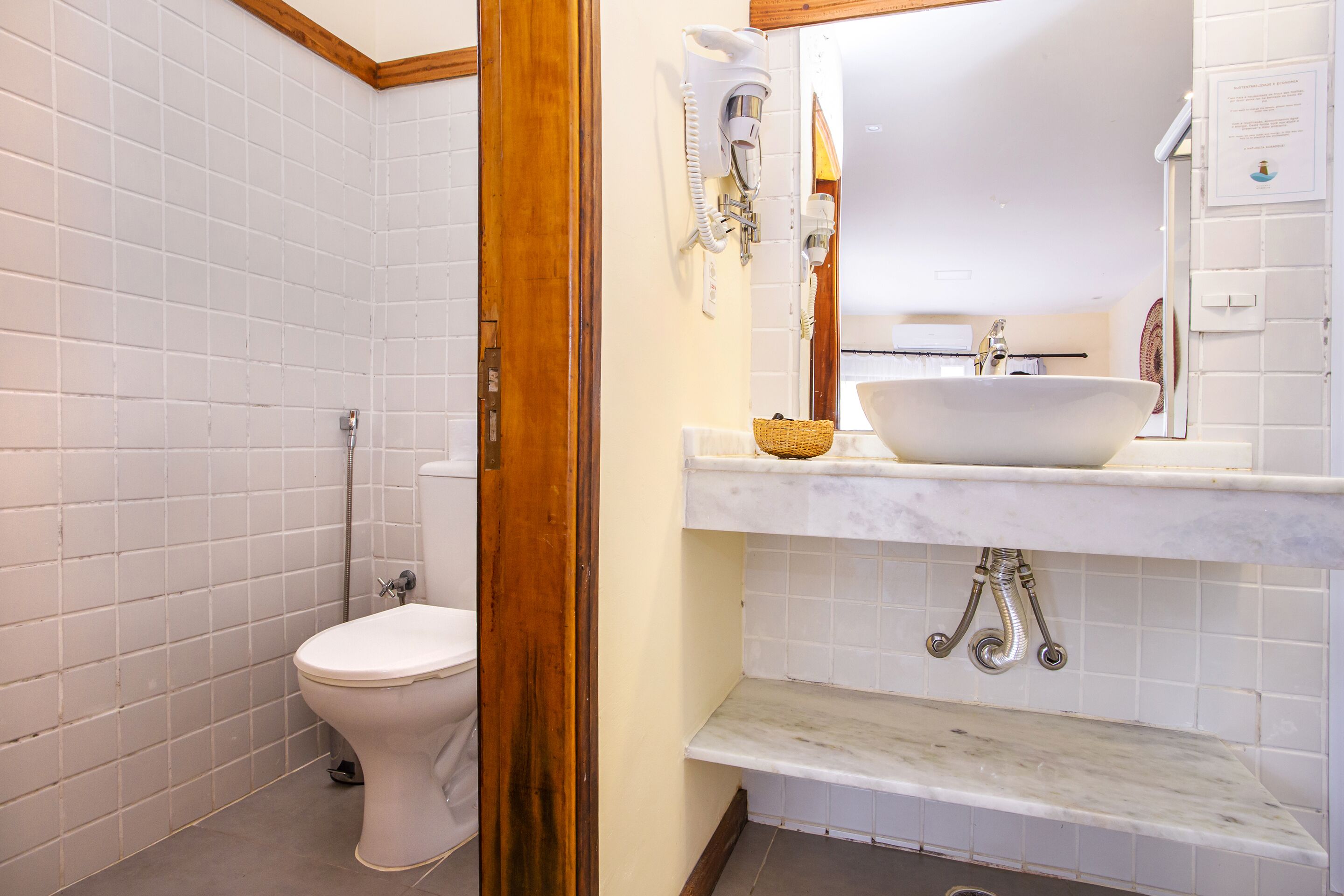 Un baño con inodoro blanco, lavamanos blanco y encimera de mármol, y zona de ducha.