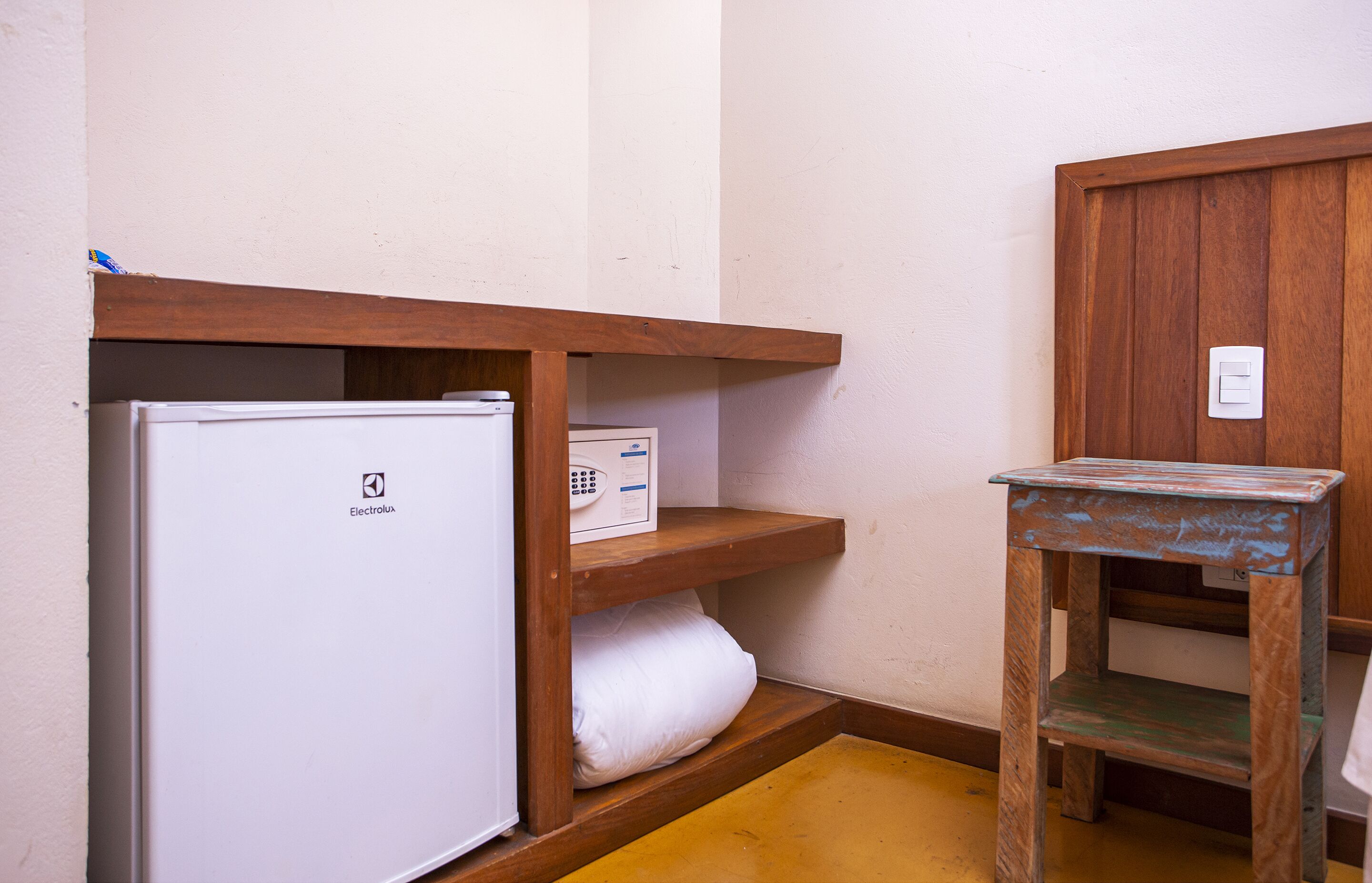 Ein kleines Zimmer mit einem weißen Kühlschrank, einer Holzregaleinheit und einem kleinen Holztisch.