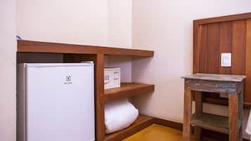 Ein kleines Zimmer mit einem weißen Kühlschrank, einer Holzregaleinheit und einem kleinen Holztisch.