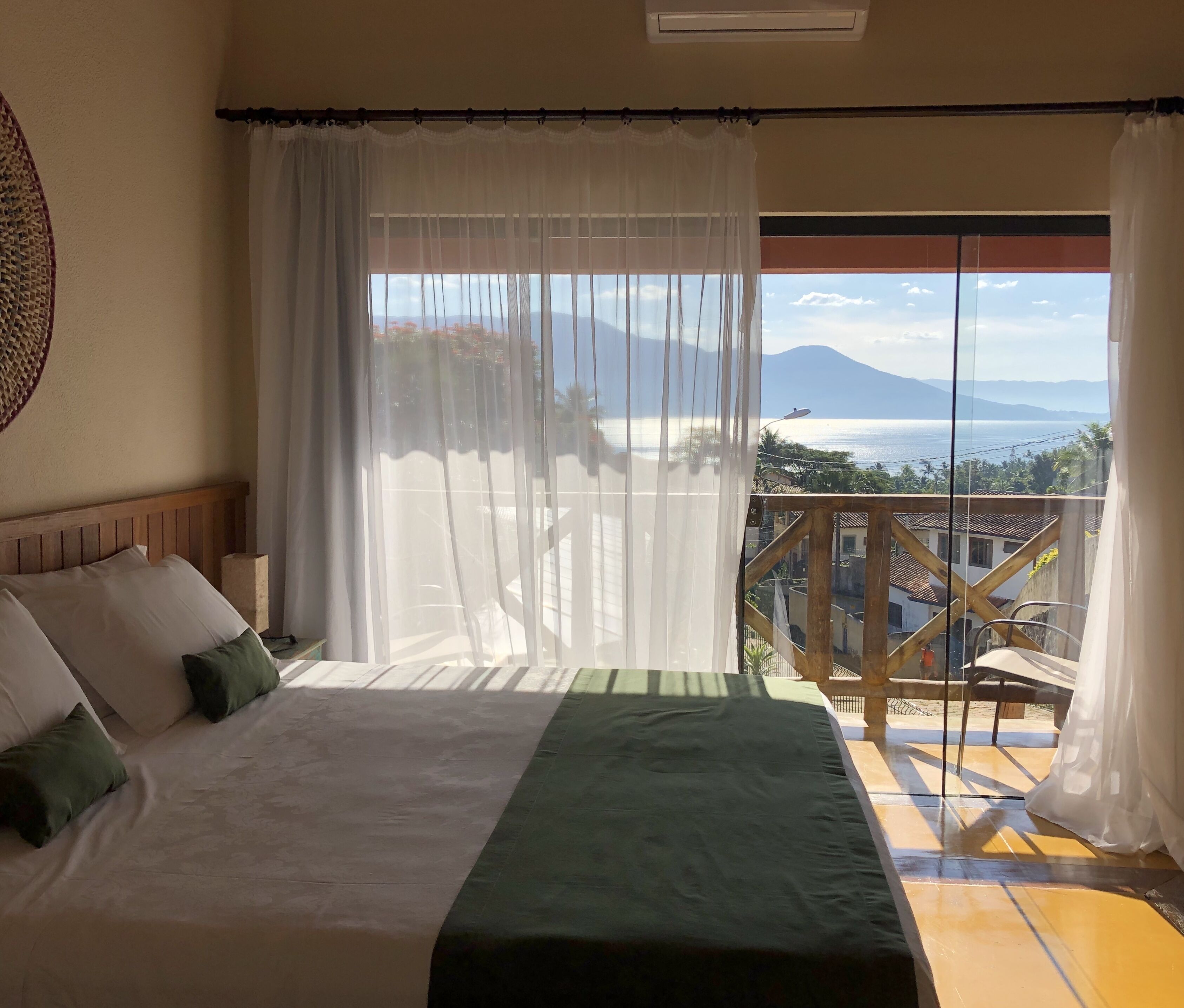 Un dormitorio con una cama grande, cortinas blancas y un balcón con vistas al mar y a las montañas.