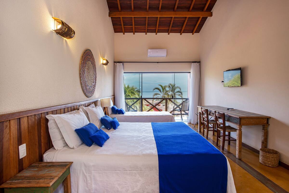 A bedroom with two beds, a wooden desk, and a balcony with a view.