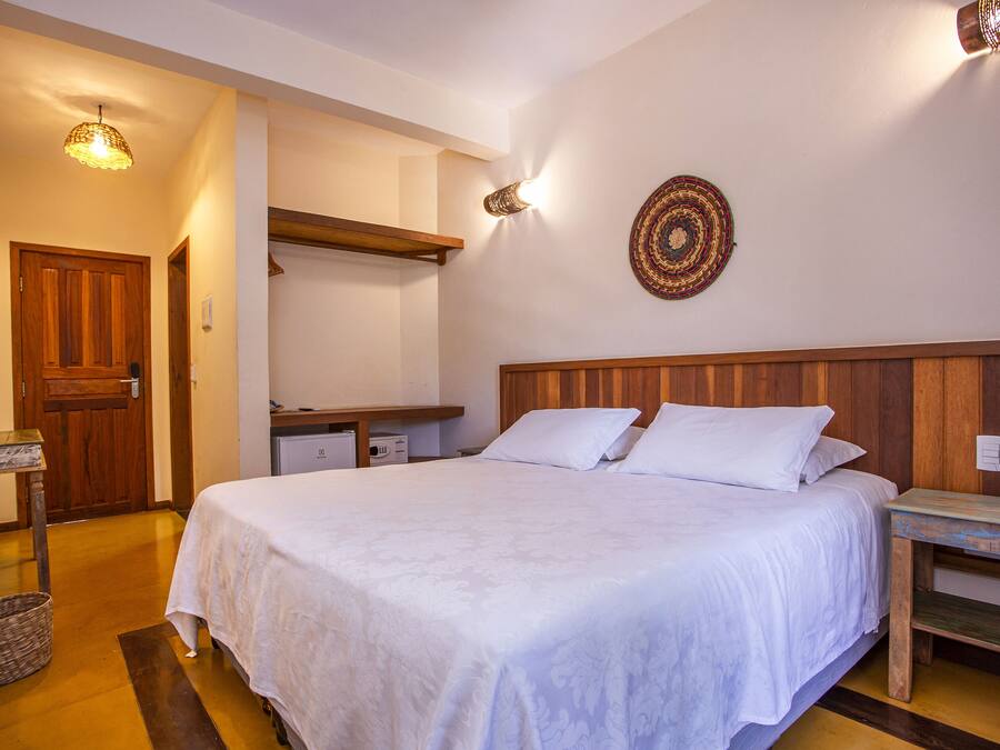 Ein Schlafzimmer mit einem hölzernen Kopfteil, einem Bett mit weißer Bettwäsche, einem Nachttisch aus Holz, einer Wandlampe und einem gewebten Korb auf dem Boden.