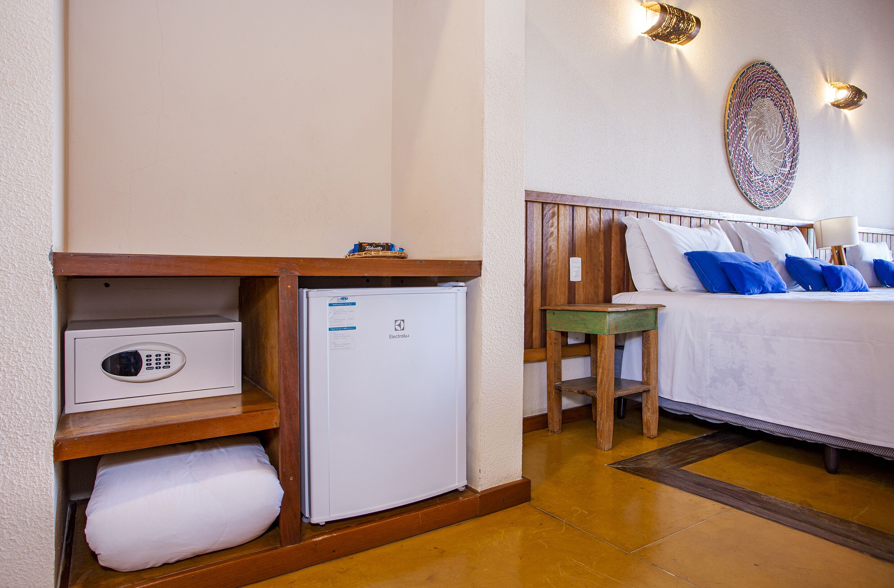 A hotel room with a bed, bedside table, and a small refrigerator.