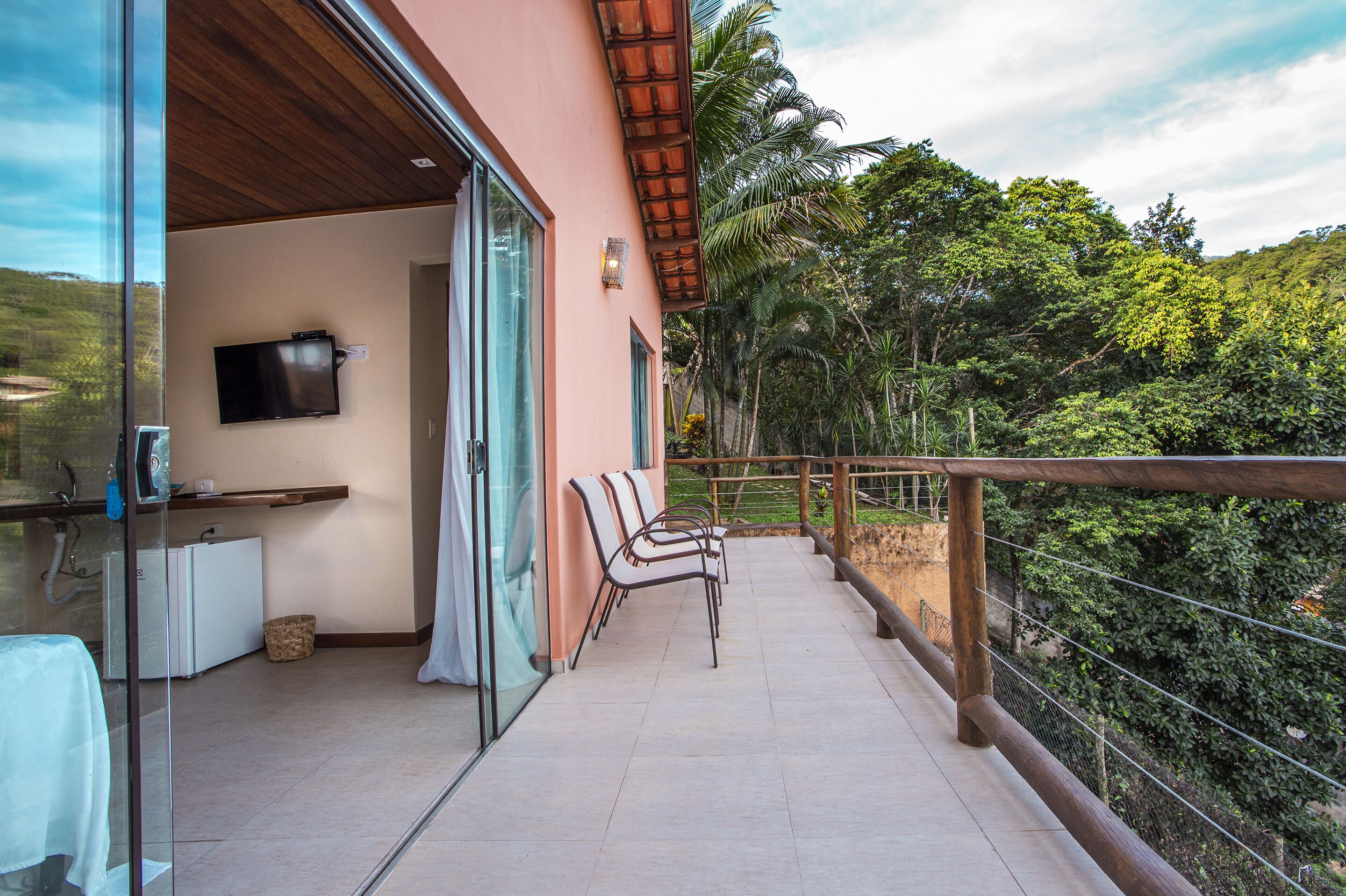 A balcony with chairs, a TV, and a view of lush greenery.