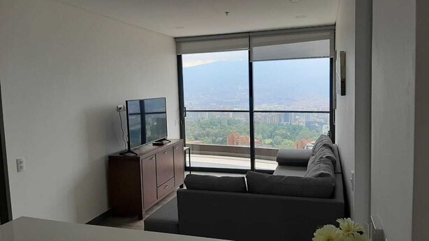 A modern living room with a large window, a flat-screen TV, a sofa, and a wooden cabinet. - ☆☆☆Contemporary Apartment with all Amenities in Balsos with City View / 1AC☆☆☆ (Medellín)