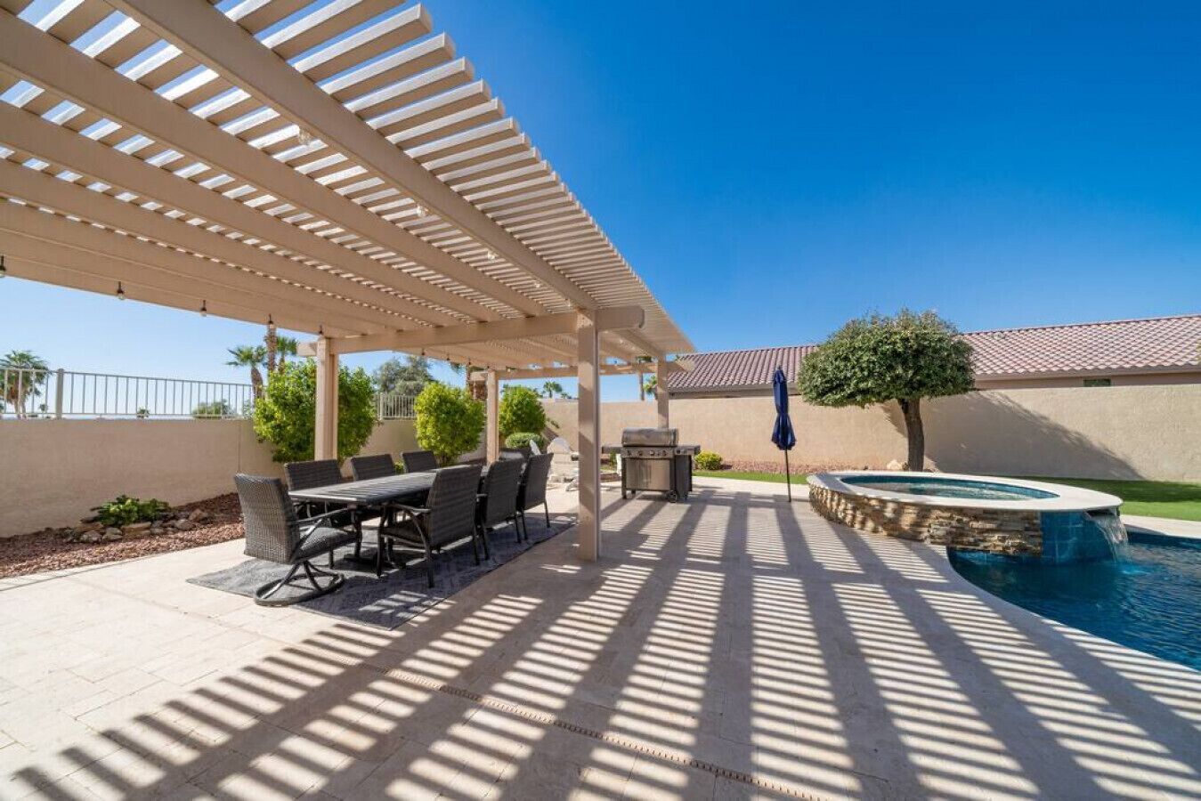An outdoor patio with a pool, covered seating area, and a barbecue grill.