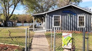 A rustic cabin with a porch, a welcome sign, and a fenced pathway leading to it. - Pop's Lakefront Retreat.<br>Remodeled clean and comfortable. (Mabank)