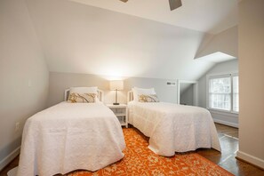 A bedroom with two beds, a nightstand, a lamp, and a window with blinds.