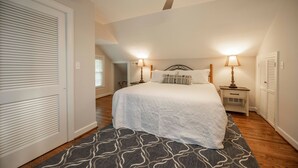 A bedroom with a bed, two bedside tables with lamps, a ceiling fan, and a patterned rug.