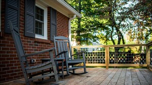 A wooden deck with two rocking chairs and a brick house with shutters.