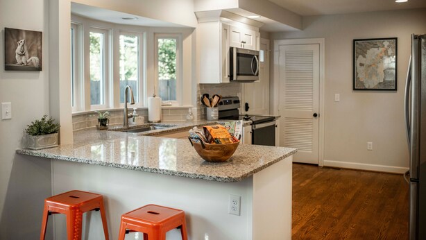 A modern kitchen with granite countertops, a central island with stools, white cabinetry, a microwave, and a refrigerator.
