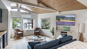 A modern living room with a large TV, comfortable seating, and a view of a lavender field. - New! Luxurious FLAT lot with private beach, dock, guest suite/apartment. (Lake Ozark)
