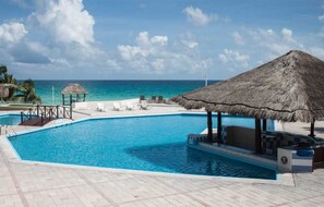 A pool with a thatched roof structure, lounge chairs, and a view of the ocean.
