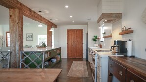 Une cuisine avec des poutres en bois, un grand îlot central et une vue sur une porte en bois.