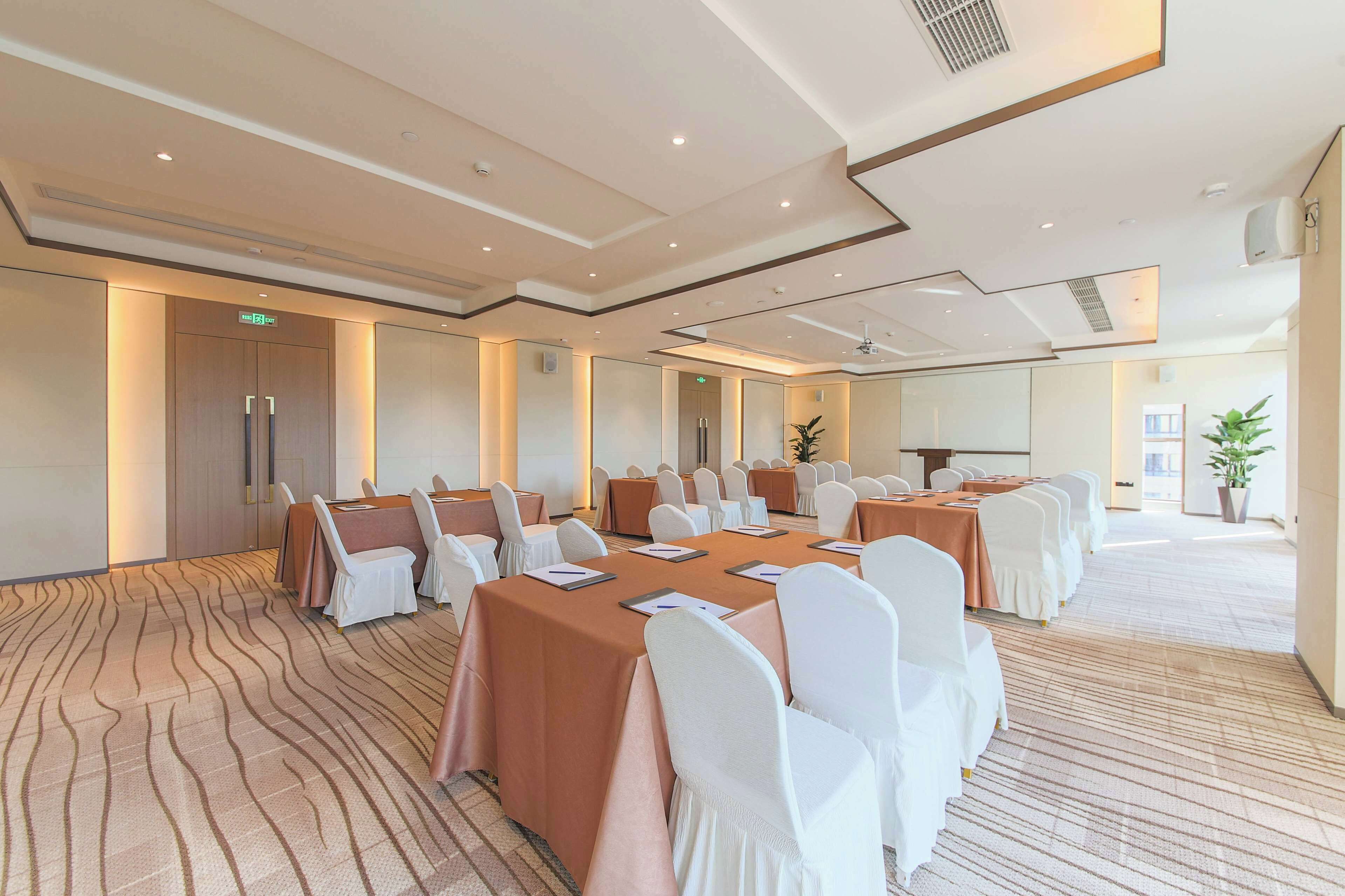 Un salón de conferencias con mesas largas, sillas blancas y una alfombra estampada.