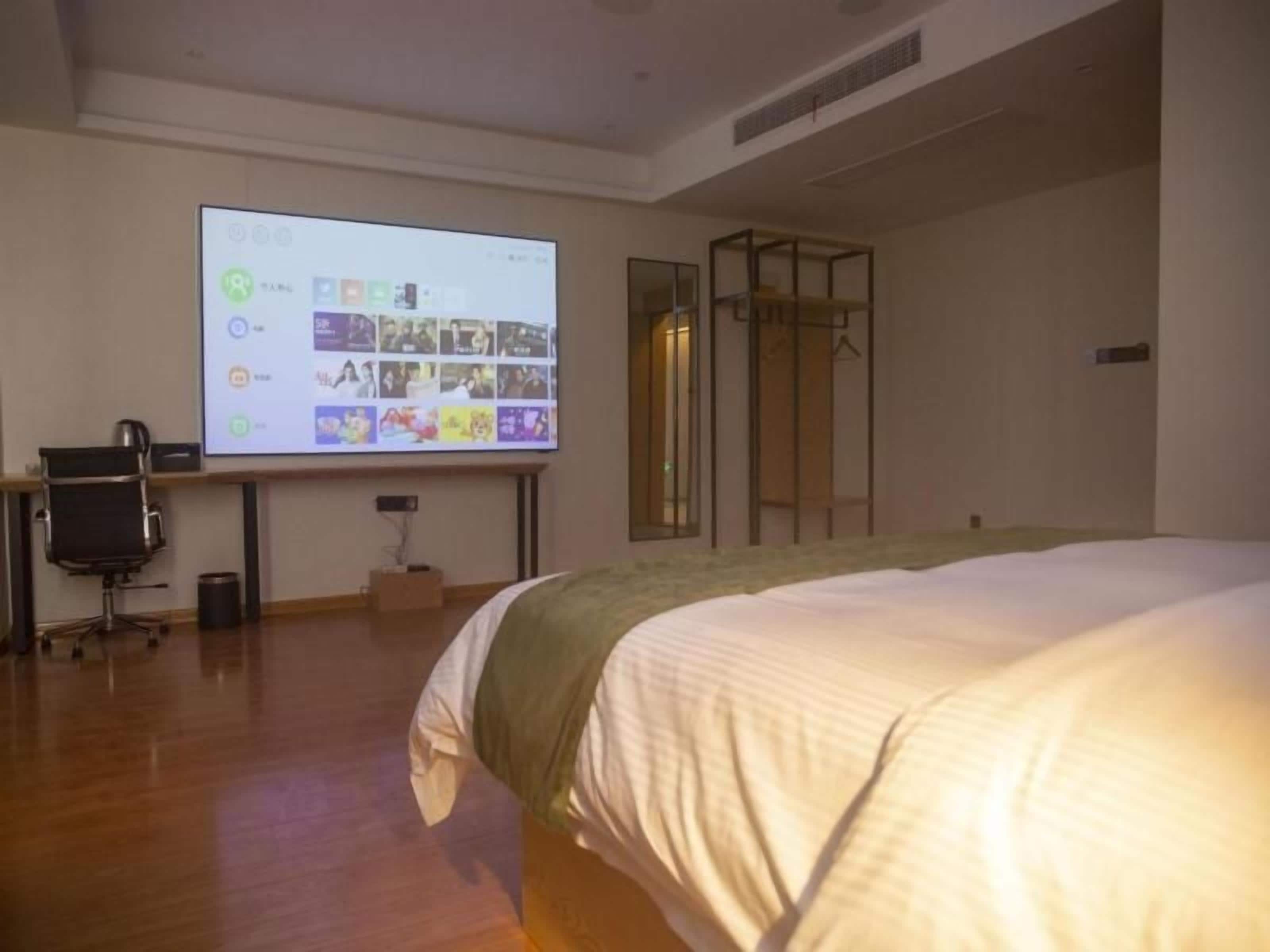 Quarto com uma cama, escrivaninha com laptop, tela de projetor e guarda-roupa.